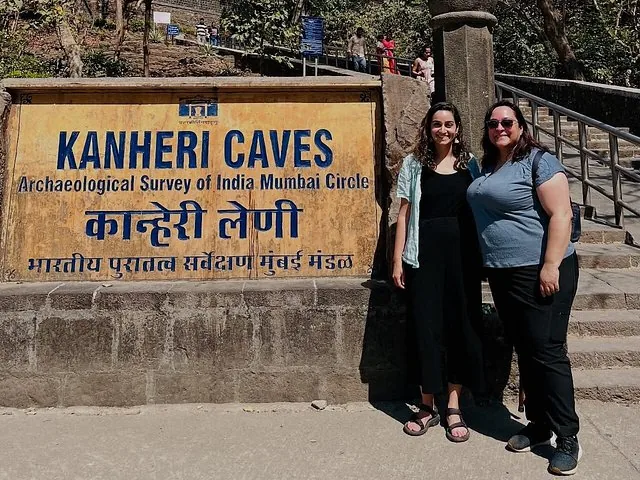 Two tourists smiling by the Kanheri Caves entrance sign